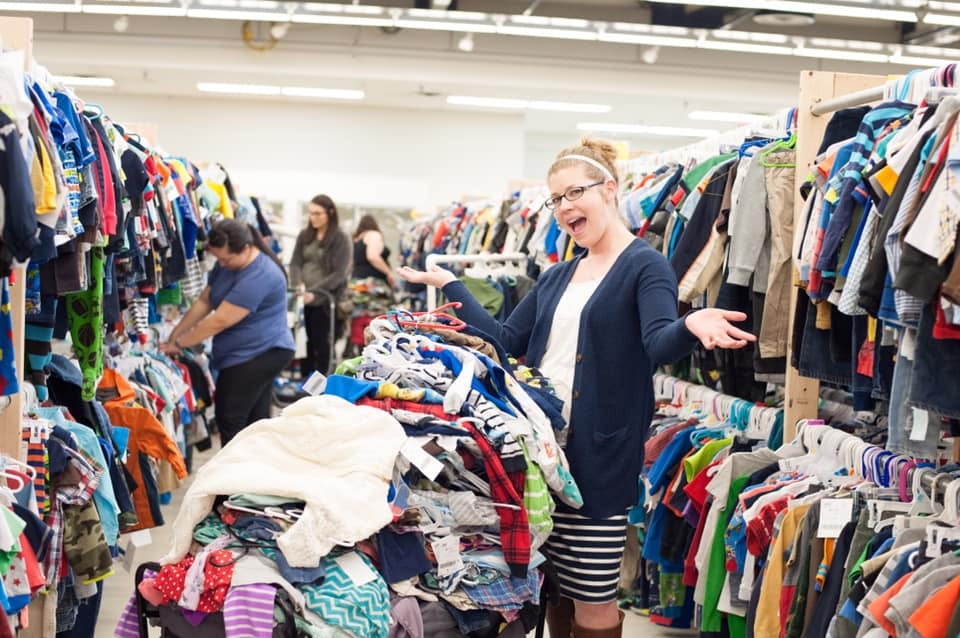 Beautiful mom holds two boys tops—one in each hand—as she shops the deals at her local sale.