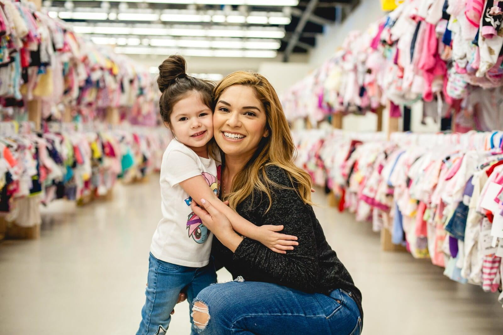 A smiling Team Member stands behind a rack of toddler girl's clothing at the sale.