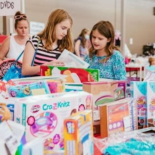 Mom holds hand up to show of rows and rows of clothing for sale at 50 to 90% off retail prices!